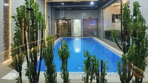 A swimming pool with a glass enclosure, surrounded by artificial plants, and a modern interior design with recessed lighting. - Villa "Milano" in Chorvoq, Tashkent (Тошкент)