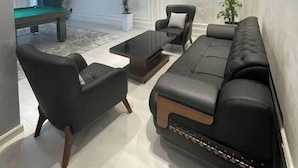 Een moderne woonkamer met een bank, fauteuils en een salontafel. In de achtergrond staat een pooltafel.