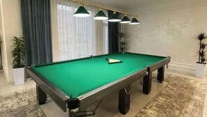 Een pooltafel in een ruimte met een hoge plafond, hanglampen en een kamerbreed tapijt.