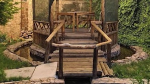 A wooden gazebo with a roof, surrounded by stone walls and greenery. - Villa "Story" in Chortoq, Tashkent (Тошкент)