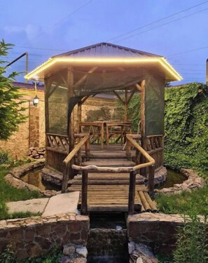 Step into a serene garden oasis with a charming gazebo featuring a wooden staircase and a soothing water feature.