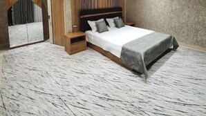 A modern bedroom with a large bed, wooden panel wall, and a small bedside table.