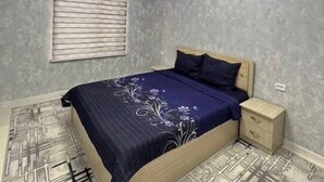 A bedroom with a bed, bedside table, and a window with blinds. - Villa "Ustoz" in Chorvoq, Tashkent (Тошкент)