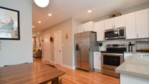 A modern kitchen with white cabinets, stainless steel appliances, and a wooden dining table. - Minutes to Downtown & Waterfronts with rooftop deck! (Baltimore)