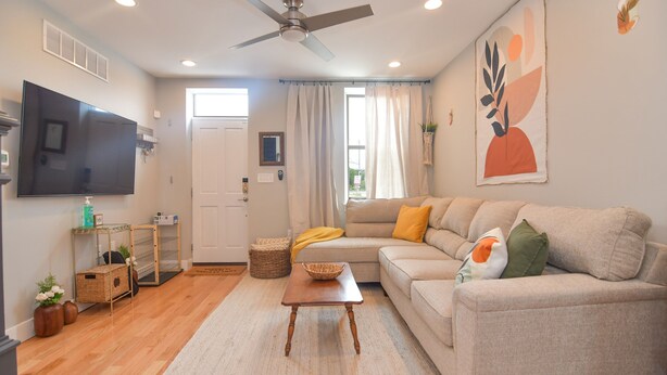 A living room with a sofa, a TV, a ceiling fan, and a window with curtains. - Minutes to Downtown & Waterfronts with rooftop deck! (Baltimore)