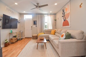 A living room with a sofa, a TV, a ceiling fan, and a window with curtains. - Minutes to Downtown & Waterfronts with rooftop deck! (Baltimore)