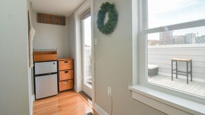 A small kitchen with a refrigerator, wooden cabinets, a window with a view of buildings, and a 'BAR' sign on the wall. - Minutes to Downtown & Waterfronts with rooftop deck! (Baltimore)