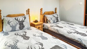 Ein Doppelbett mit Hirschmuster, ein Nachttisch mit Lampe und ein Bild an der Wand.
