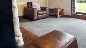 A living room with a brown leather sofa, a wooden coffee table, and a flat-screen TV mounted on the wall.