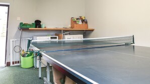 Ein Tischtennis-Tisch in einem Raum mit Heizkörper, einem grünen Korb und einem Regal mit verschiedenen Gegenständen.