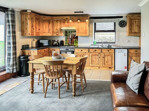 Una cocina con armarios de madera, una mesa de comedor con sillas, un refrigerador y una ventana con vistas a la vegetación.