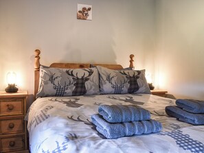 A bedroom with a bed, two pillows with deer patterns, a bedside table with a lamp, and a drawer unit.