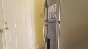 Eine Küche mit einem Edelstahl-Kühlschrank, einer weißen Tür und einem Mülleimer.
