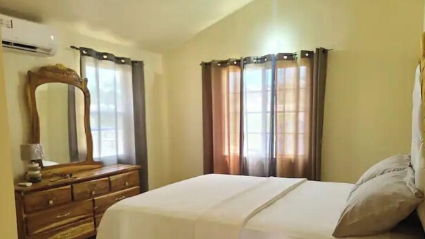 Ein Schlafzimmer mit Bett, Kommode, Spiegel und Vorhängen.