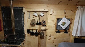 L’intérieur chaleureux d’un chalet avec un poêle à bois, des étagères remplies d’ustensiles de cuisine et un lit recouvert d’une couverture blanche.