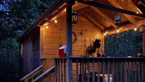Une cabane en bois avec une véranda, un petit escalier et des guirlandes lumineuses.