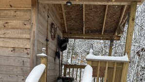 Une cabane en bois dotée d’un porche couvert et d’un escalier menant à l’entrée, le tout entouré de neige.