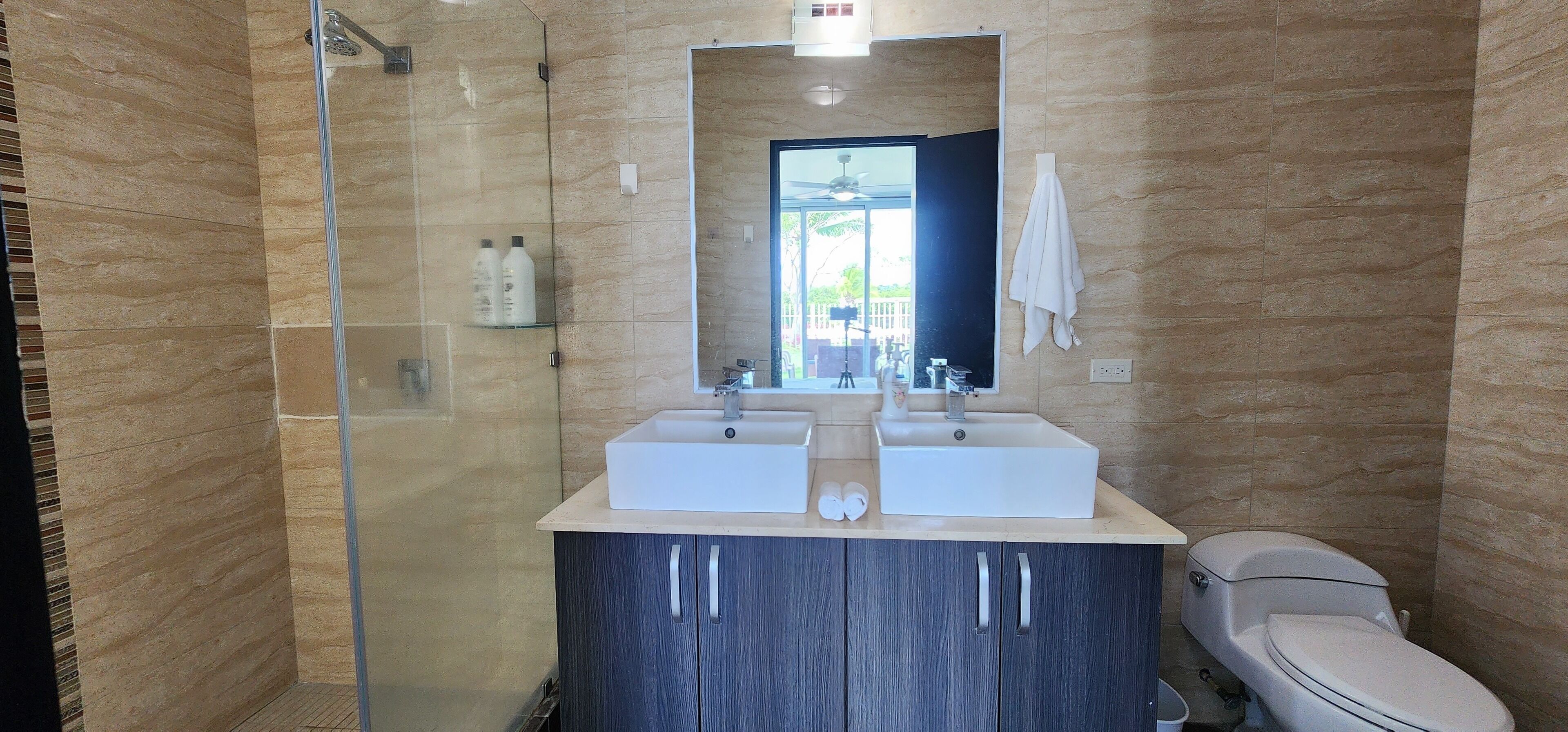 A modern bathroom with two sinks, a glass shower enclosure, and a toilet.