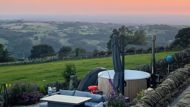 A scenic outdoor seating area with a view of rolling hills, a stone wall, and a hot tub.