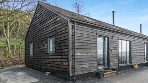 A wooden cabin with a pitched roof, a chimney, and a door leading to a covered porch.
