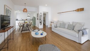 Una sala de estar moderna con un sofá blanco, un comedor con mesa y sillas, un televisor y una pala de madera en la pared.