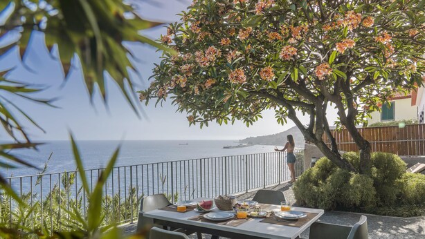 Un área de comedor al aire libre con una mesa preparada para dos, con vista a un cuerpo de agua y la costa.