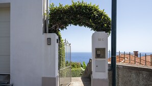 Una entrada protegida por un muro con vistas al mar, una placa de número y una verja de metal.