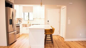 A modern kitchen with a stainless steel refrigerator, white cabinetry, and a wooden floor. - The Duffer's Drop - 2BR/2BA Condo in Pinehurst, NC (Pinehurst)