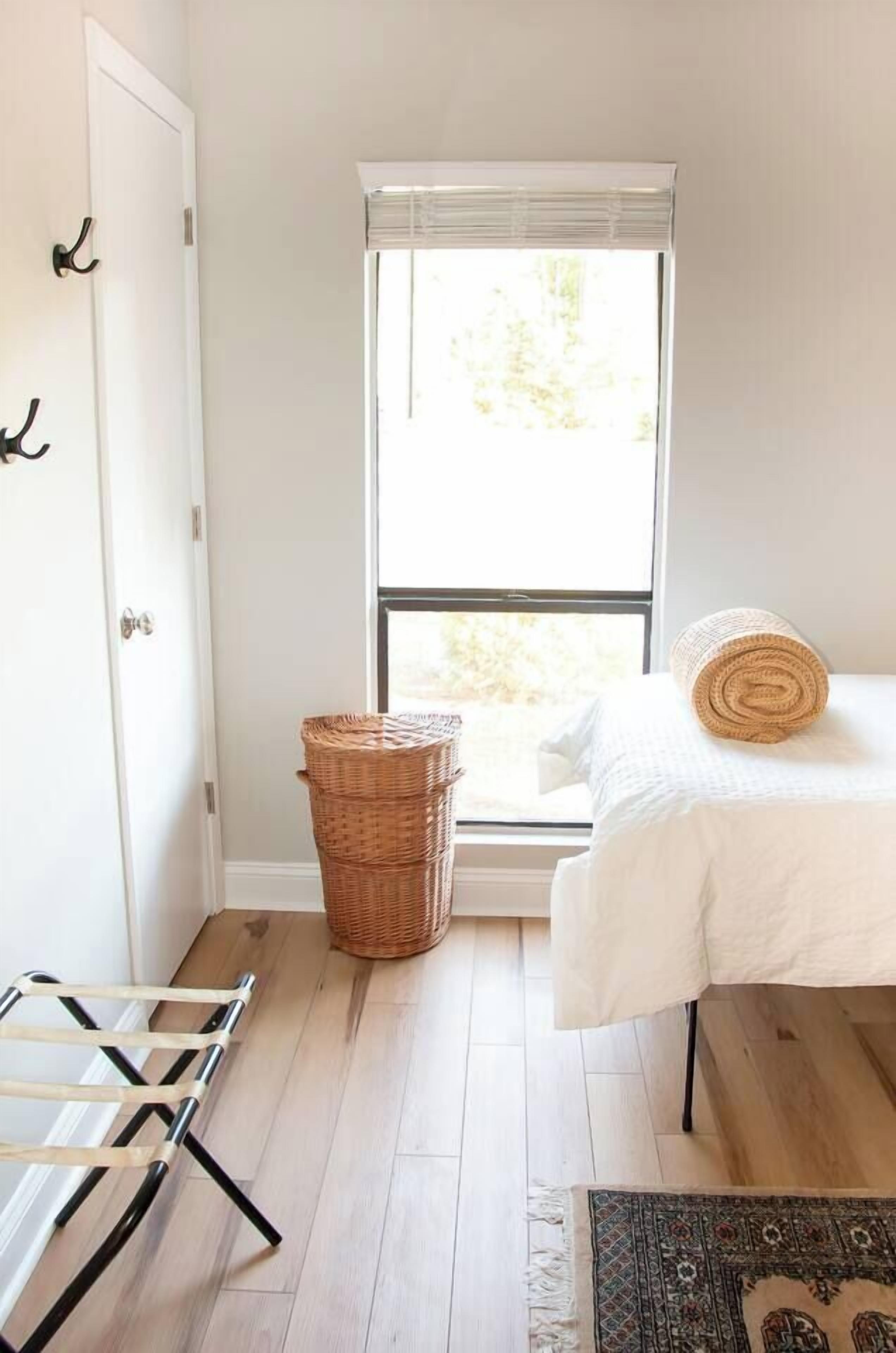 Ein Zimmer mit Bett, Fenster, einem Korbwäschesystem, einer Wäscheständer und einem gemusterten Teppich.