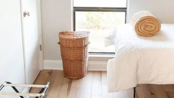 Ein Zimmer mit Bett, Fenster, einem Korbwäschesystem, einer Wäscheständer und einem gemusterten Teppich.