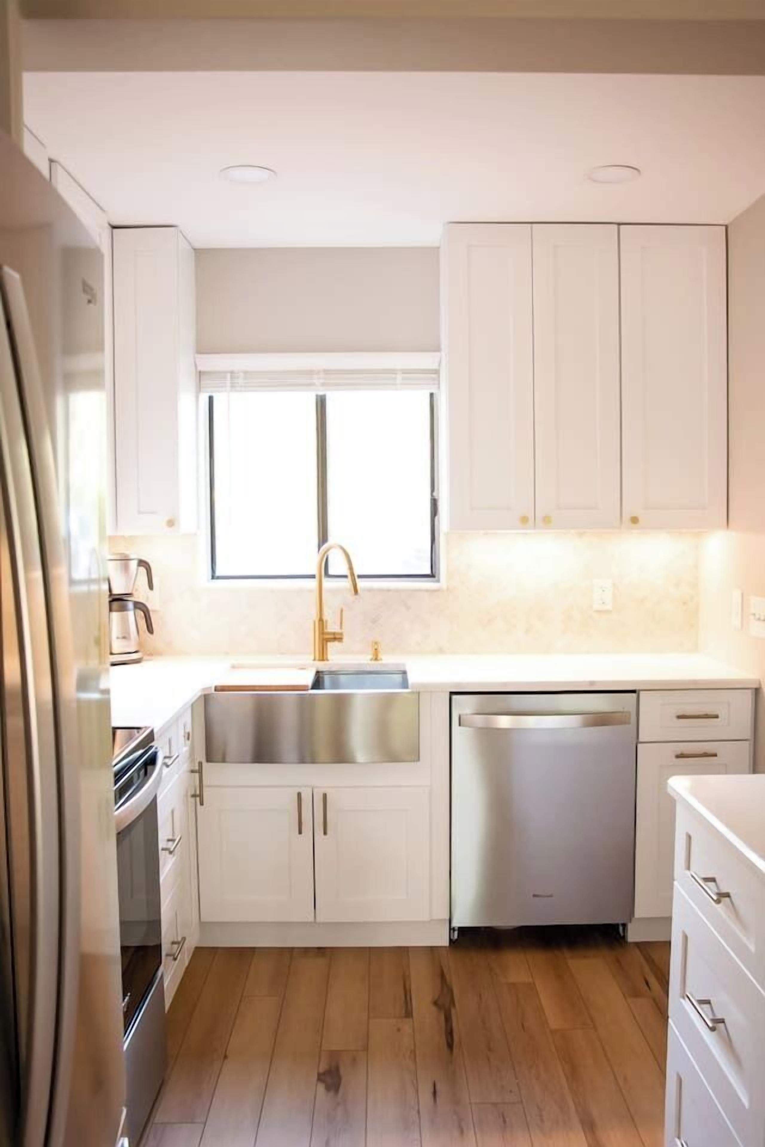 Una cocina moderna con armarios blancos, electrodomésticos de acero inoxidable y piso de madera.
