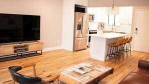 A modern kitchen with stainless steel appliances, a central island with bar stools, and a wooden dining table with chairs. - The Duffer's Drop - 2BR/2BA Condo in Pinehurst, NC (Pinehurst)