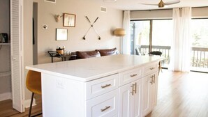 A modern kitchen with a large island, white cabinetry, and a dining area with a table and chairs. - The Duffer's Drop - 2BR/2BA Condo in Pinehurst, NC (Pinehurst)