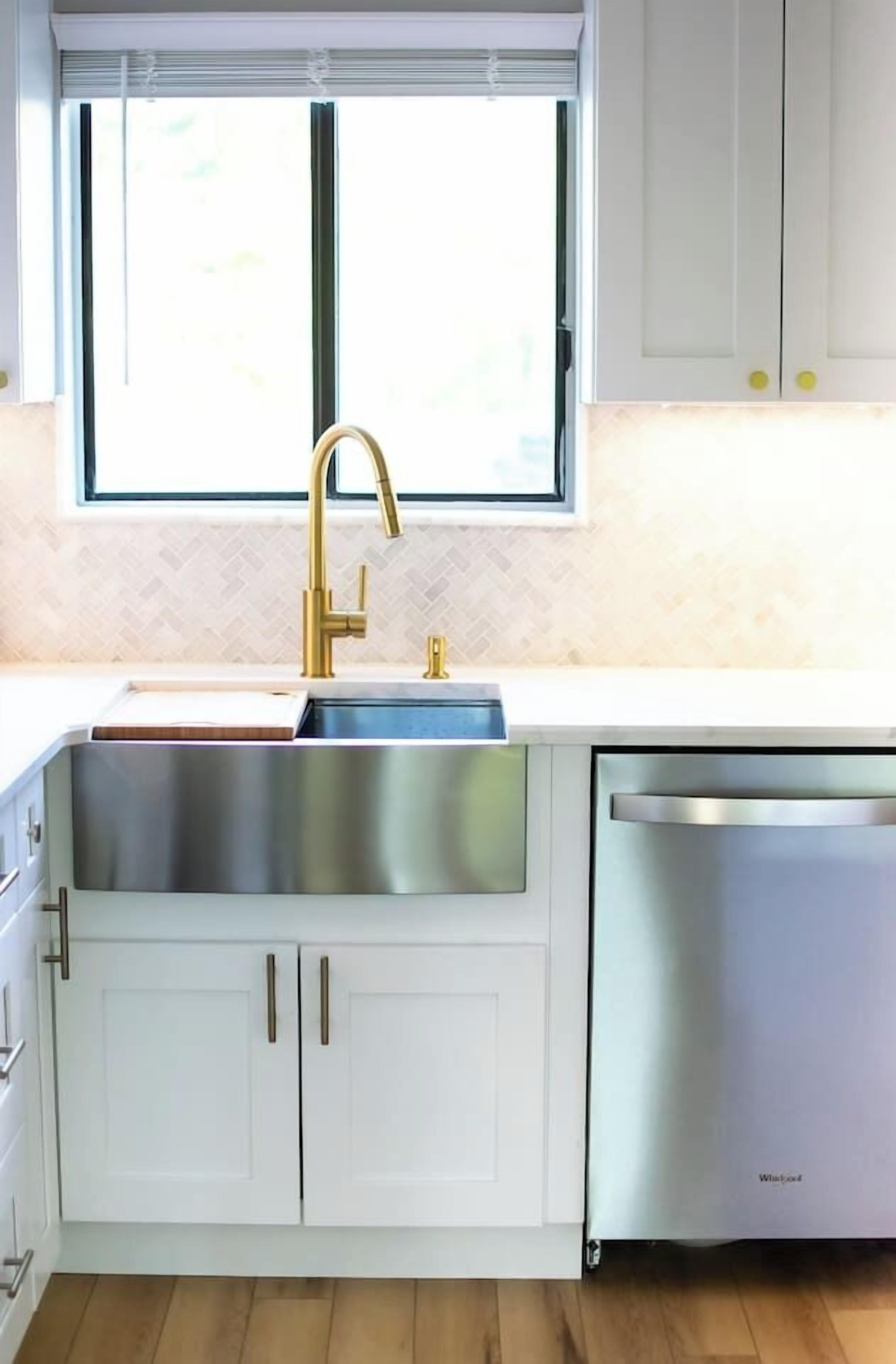 A modern kitchen with a stainless steel sink, gold faucet, white cabinets, and a built-in dishwasher.