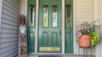 A green door with a 'WELCOME' sign, a doormat, and a potted plant on a stand.