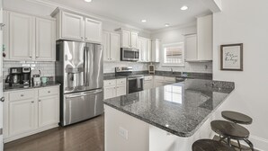A modern kitchen with white cabinets, stainless steel appliances, granite countertops, and a central island with stools. - Resort Pool - Firepit - Sleeps 10 (Santa Rosa Beach)