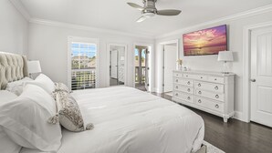 A bedroom with a large bed, a ceiling fan, a dresser, and a painting of a sunset. - Resort Pool - Firepit - Sleeps 10 (Santa Rosa Beach)
