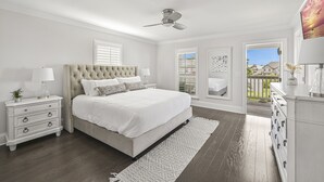 A bedroom with a large bed, a ceiling fan, a nightstand with a lamp, a dresser, and a view of the outside through a window. - Resort Pool - Firepit - Sleeps 10 (Santa Rosa Beach)