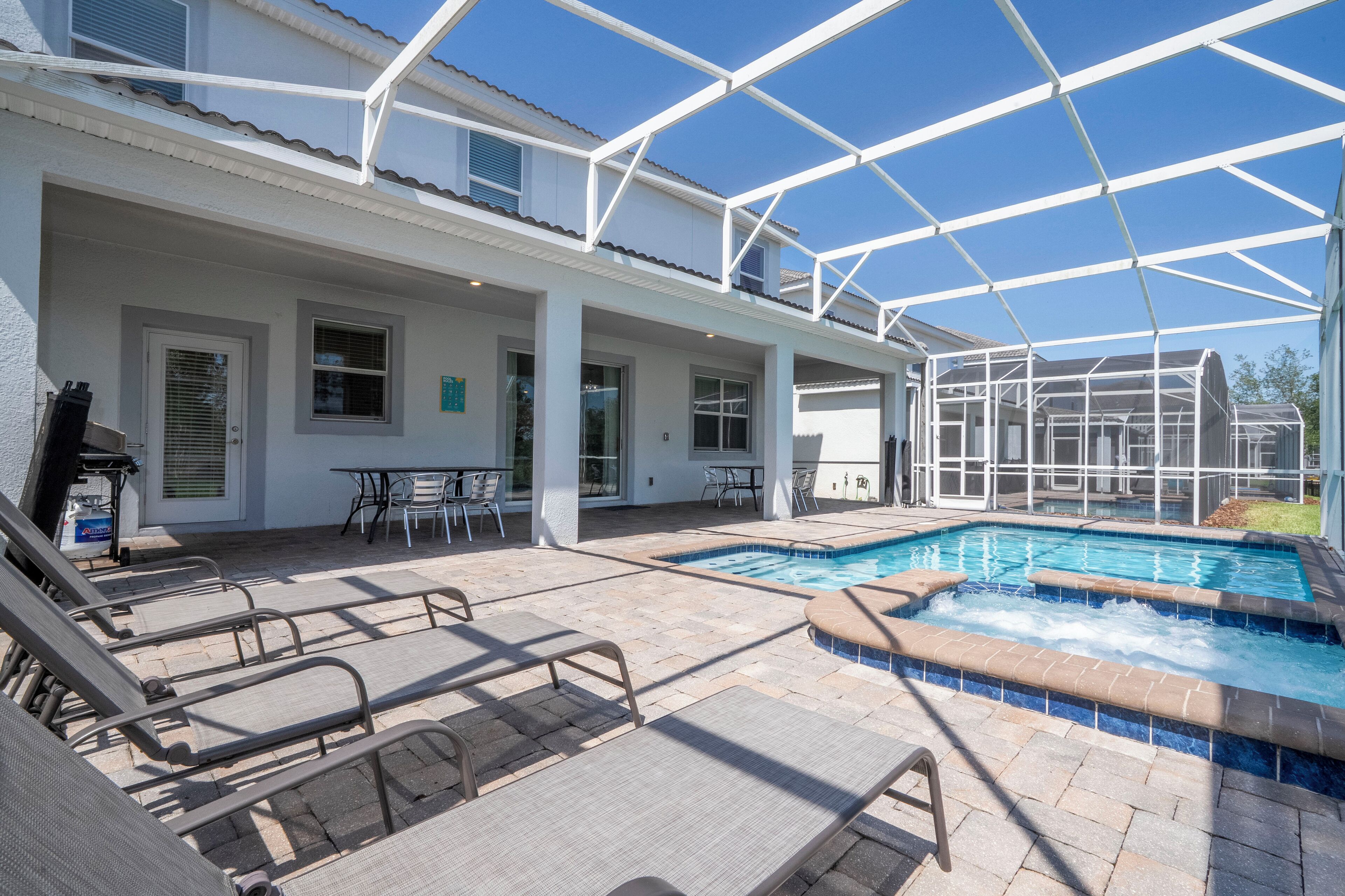 A covered outdoor pool area with lounge chairs and a hot tub.
