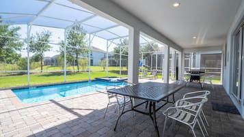 A covered outdoor area with a pool, patio furniture, and a grill.