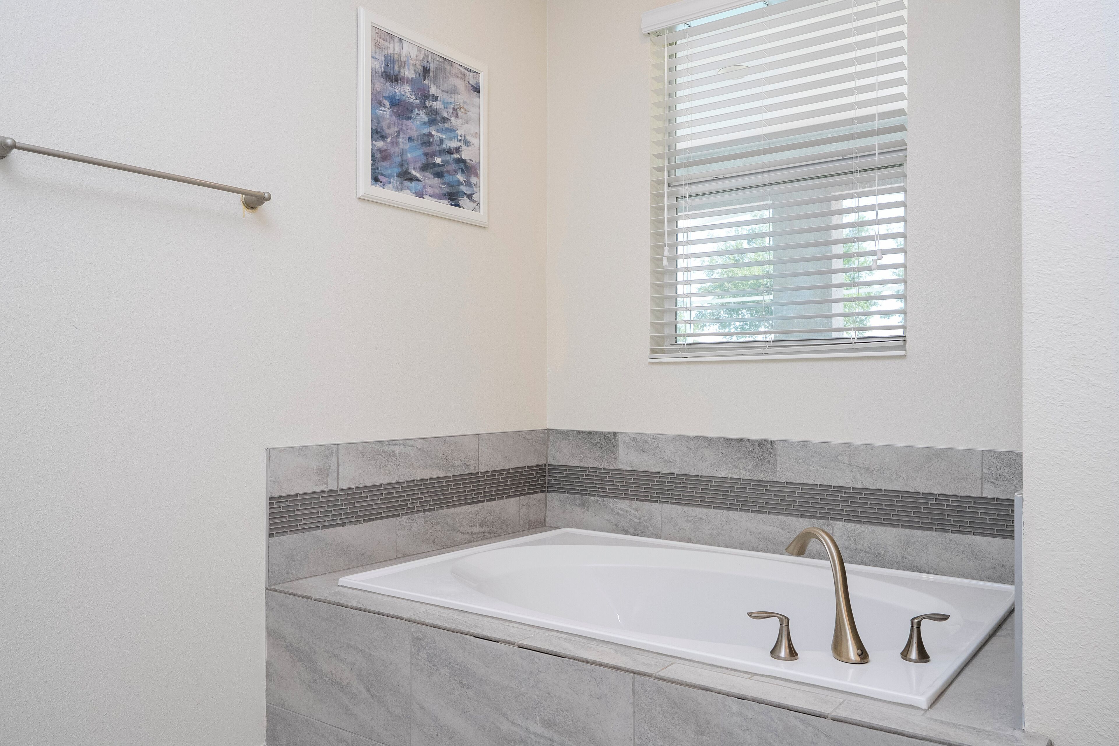 Un baño con una bañera blanca, un perchero, una ventana con persianas y un salpicadero de azulejos.