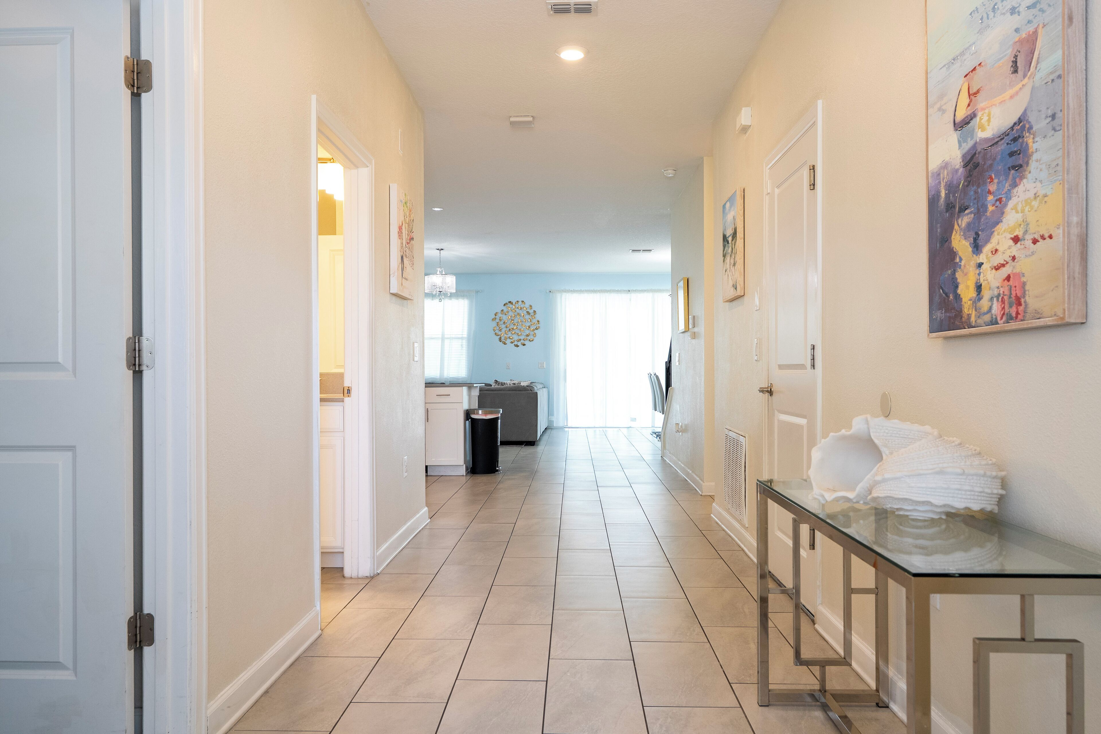 A hallway with a glass-top table, a trash can, and a painting on the wall.