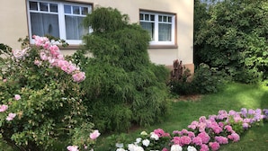 A building with two windows, surrounded by a well-maintained garden with various flowering plants. - Vacation home Beerster Sonne Ideal for a long stay (Gestland)