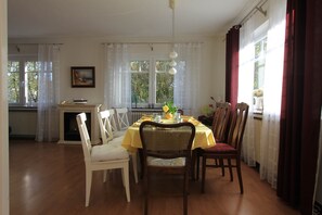 Ein Esszimmer mit Tisch für vier Personen, umgeben von Stühlen, einem Kamin und großen Fenstern mit Vorhängen.