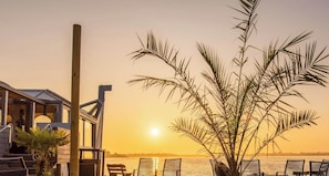 Ein Strandgrundstück mit Holzstruktur, einer Palme und Blick auf den Sonnenuntergang über dem Wasser.