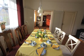 Ein Esszimmer mit Tisch für vier Personen, Stühlen, einer Blumenvase und einem Fenster mit Vorhängen.