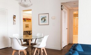Une pièce moderne avec une table à manger en verre entourée de chaises blanches, un canapé bleu et un tableau encadré au mur.