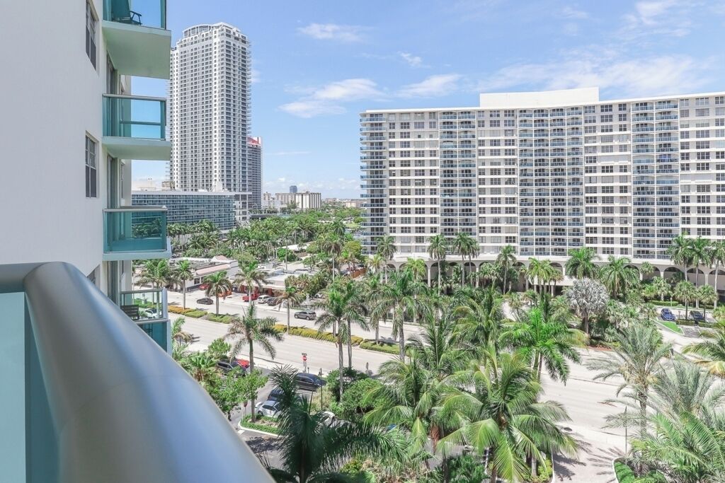 A high-rise hotel with multiple floors, a parking area, and a landscaped courtyard with palm trees.