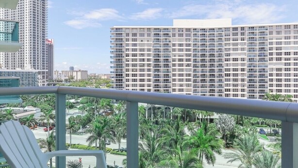 A balcony with a white chair, overlooking a cityscape with tall buildings and palm trees. - Komffy Apt w/2 Queen Beds and Canal View at Tides (Hollywood)