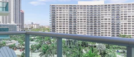 A balcony with a white chair, overlooking a cityscape with tall buildings and palm trees.